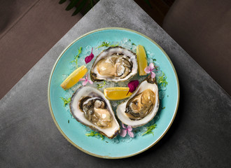 Oysters in ice with flowers and lemon on a blue plate