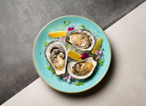 Oysters in ice with flowers and lemon on a blue plate