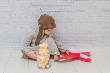 girl, child in the helmet of the pilot with the aircraft and lights in the glass in front of a white brick wall