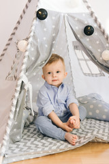 Cute one year old baby playing in a tent, wigwam. Shadow depth of field, natural light. The interior of the children's room is grey, blue and white