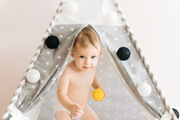 Naked one year old baby plays tent, wigwam closing his eyes with his hands shadow depth of field, natural light. The interior of the children's room is grey, blue and white © ksyusha_yanovich