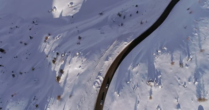 Overhead vertical aerial above snowy road following cars.Sunny sunset or sunrise.Winter Dolomites Italian Alps mountains outdoor nature establisher.4k drone flight establishing shot