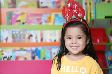 asian child or kid girl smile and wear red antler reindeer hair band or santa claus suit or santie for christmas or xmas and happy new year festival with fun on winter season and tale shelf background