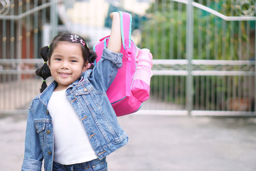 Asian child or kid girl smile and student holding and show pink schoolbag for committed determine with happy on go to school or back to school and kindergarten from summer study or learning to home