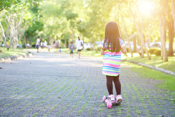 asian child or kid girl funny and playing or riding pink scooter for exercise with healthy and balance learning with training on holiday relax and family day at public park or green garden on sunlight