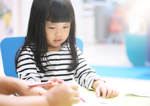 Asian child cute or kid girl smile and study learning for coloring paint on white paper with teacher or mother at nursery or children pre school and kindergarten on soft focus and sunlight on window