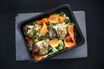 Lunch box.
Roladki z grillowanego bakłażana z suszonymi pomidorami i serem podane na sałacie i marchewce zapakowane w pojemnik na żywność.

