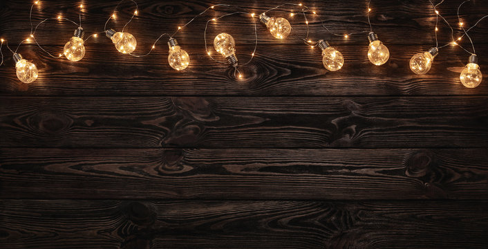 Empty, dark wooden background illuminated by retro light bulbs, with copy space