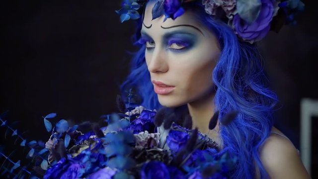 beautiful girl model with creative makeup for Halloween in the style of the bride's corpse stands in the Studio on a black background with a bouquet of blue flowers