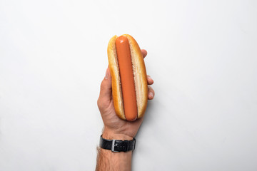 cropped shot of man holding tasty hot dog on white marble surface