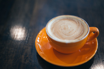 A orange cup of coffee on wooden background