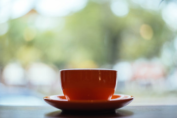 A orange cup of coffee on wooden background in coffee shop