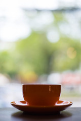 A orange cup of coffee on wooden background in coffee shop