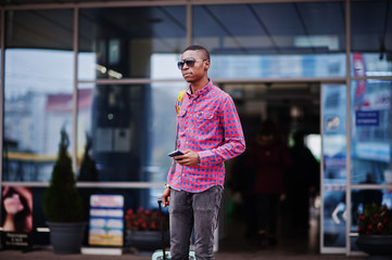 African american man in checkered shirt, with suitcase and backpack. Black man traveler against bus...