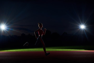 Silhouette of woman running forward in darkness on stadium.