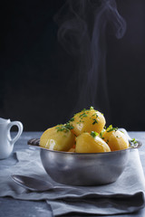 Hot boiled potatoes in a plate dusted with greens and smoke on a gray background