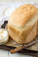 Homemade freshly baked bread on an old cast-iron baking sheet, next to a knife and a jar of butter. 