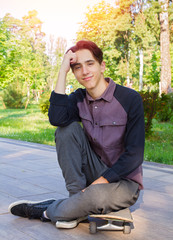 Young man sitting and relaxing on skateboard after skating in city park. Teen boy skater