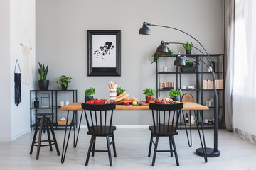 Black chairs at wooden table with food in grey dining room interior with poster and lamp. Real photo