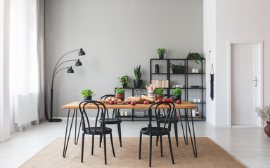 Black chairs at wooden table with food in grey dining room interior with plants and lamp. Real photo