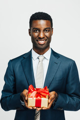 Vertical portrait of a smiling man holding a golden gift tied with a  red ribbon, isolated on white studio background