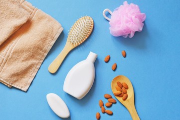 Flat lay organic bath products. Beige terry towel, hair brush, shampoo, soap, pink sponge and almonds on a blue background