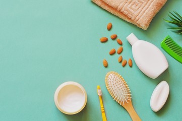Flat lay photo almond oil based cosmetics. Natural cream, organic shampoo, hairbrush, soap bar, beige towel on a green background