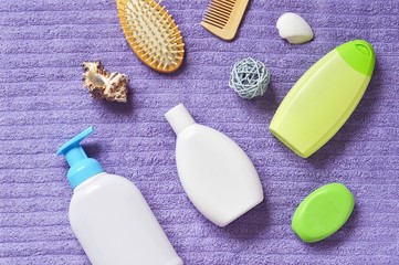 Shampoo, shower gel, liquid soap, purple terry towel, seashells view from above. Flat lay bathroom items