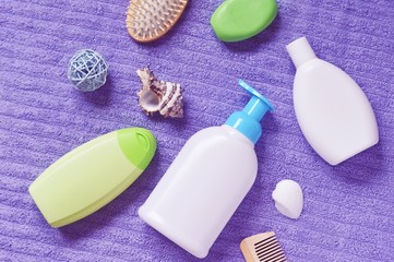 Flat lay photo toiletries on a purple fluffy towel. Green shampoo bottle, liquid soap, shower gel and hair brush
