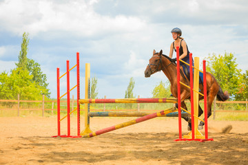 Jockey young girl doing horse jumping through hurdle
