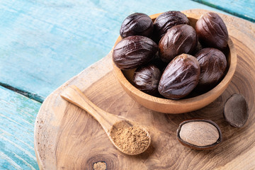 Whole inshell nutmeg nuts in a bowl and a spoon with nut powder on blue rustic wooden table.
