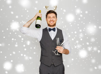 celebration, christmas and holidays concept - happy man with bottle of champagne and wine glasses at new year party over grey background and snow