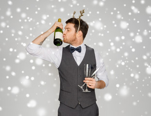 celebration, people and holidays concept - happy man kissing bottle of champagne and wine glasses at christmas or new year party over grey background and snow