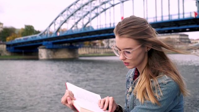 Young, pretty teen girl reading book in the city, super slow motion
