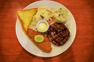 grill pork and fried fish steak with salad, fried rice and butter bread on table