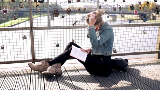 Young, pretty woman reading book sitting on the bridge in the city
