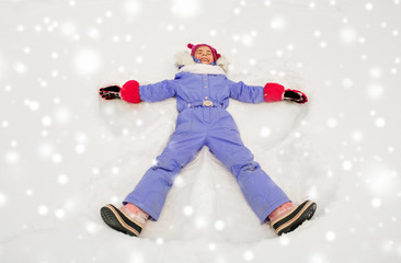 Fototapeta na wymiar childhood, leisure and season concept - happy little girl in winter clothes making snow angels outdoors