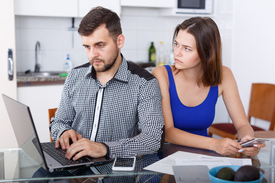 Young man working at laptop and upset girl using phone at home