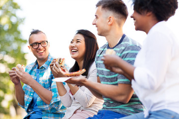 people, fast food and international concept - happy friends eating sandwiches and pizza outdoors