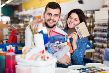 Young active couple demonstrating tools for house renovating in paint store