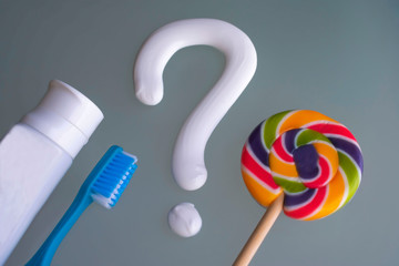 Question mark from toothpaste, toothbrush, closed paste tube, colorful lollipop on blue background. Concept of dental care.