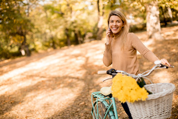 Young woman with bicycle using smartphone in autumn park