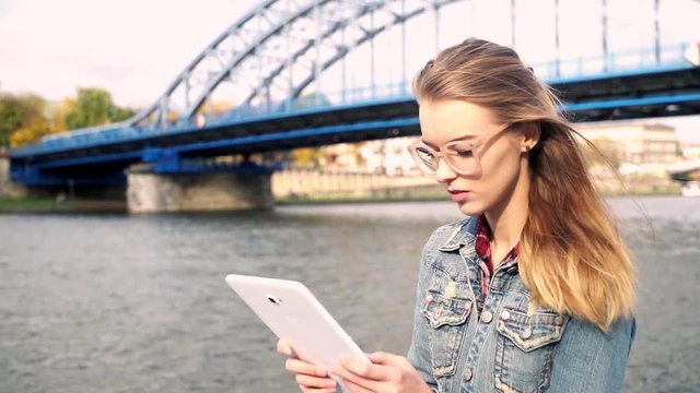 Young teen girl standing with tablet on the bridge in the city, super slow motion
