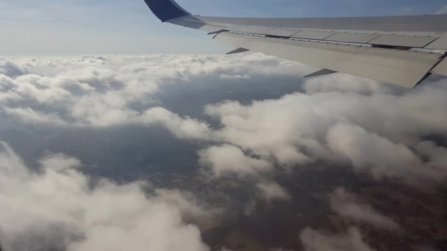POV-Aircraft wing flying over broken cloud layer as it departs from London's Heathrow airport with English countryside far below.