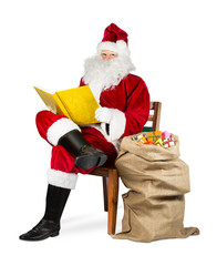 Traditional red white Santa claus reading golden book with gift bag on chair isolated on white xmas christmas background 
