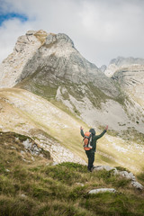 Hiking man with backpacker open arms looking mountain peaks
