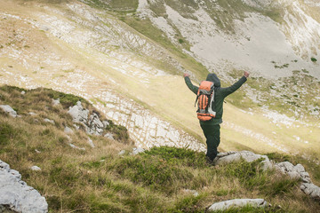 Hiking man with backpacker open arms looking mountain peaks