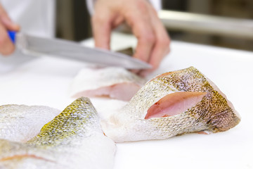 A chef scoring a zander fish fillets with a knife. White chopping board.