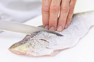 A chef scoring a large zander fish fillet with a knife. White chopping board.