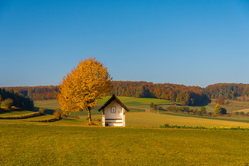 Plakat Small chapel on the left side in autumn landscape and with colorful foliage